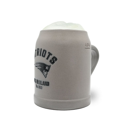 Grauer PREMIUM Teamkrug New England Patriots aus Steinzeug mit Logo und 0,5 Liter Markierung, gefüllt mit Schaum.