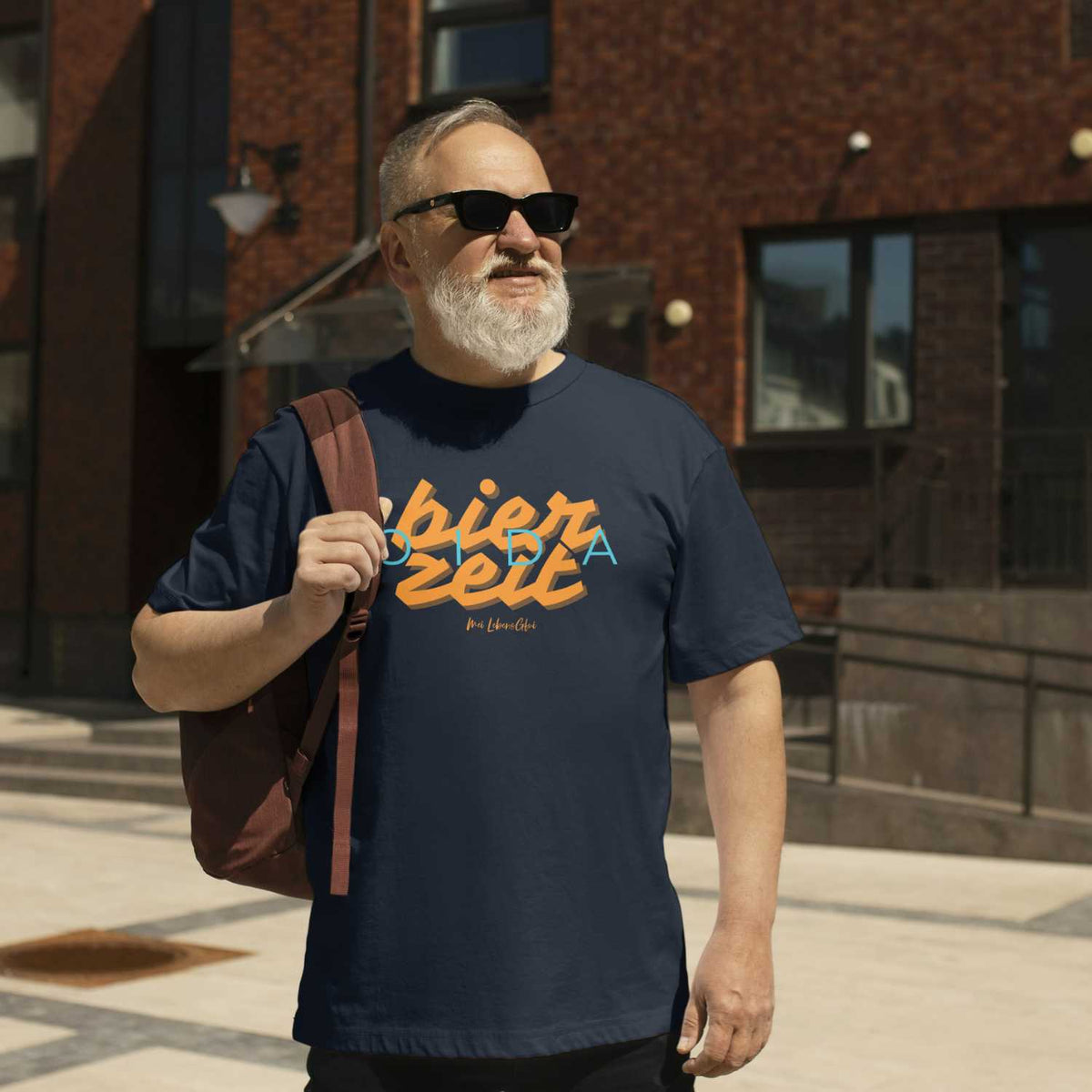 Mann mit grauem Bart und Sonnenbrille trägt marineblaues Herren T-Shirt Bierzeit mit Aufdruck auf der Straße.