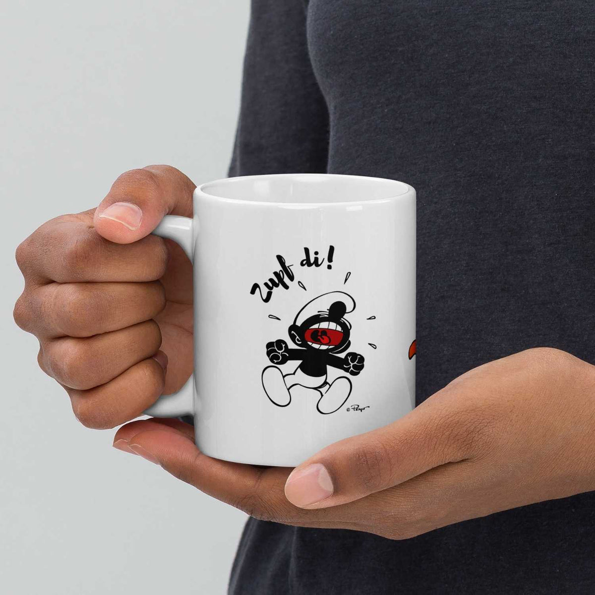 Schlumpf Tasse Zupf di! in Händen gehalten, mit schwarzem, schreiendem Schlumpf-Motiv und Schriftzug.