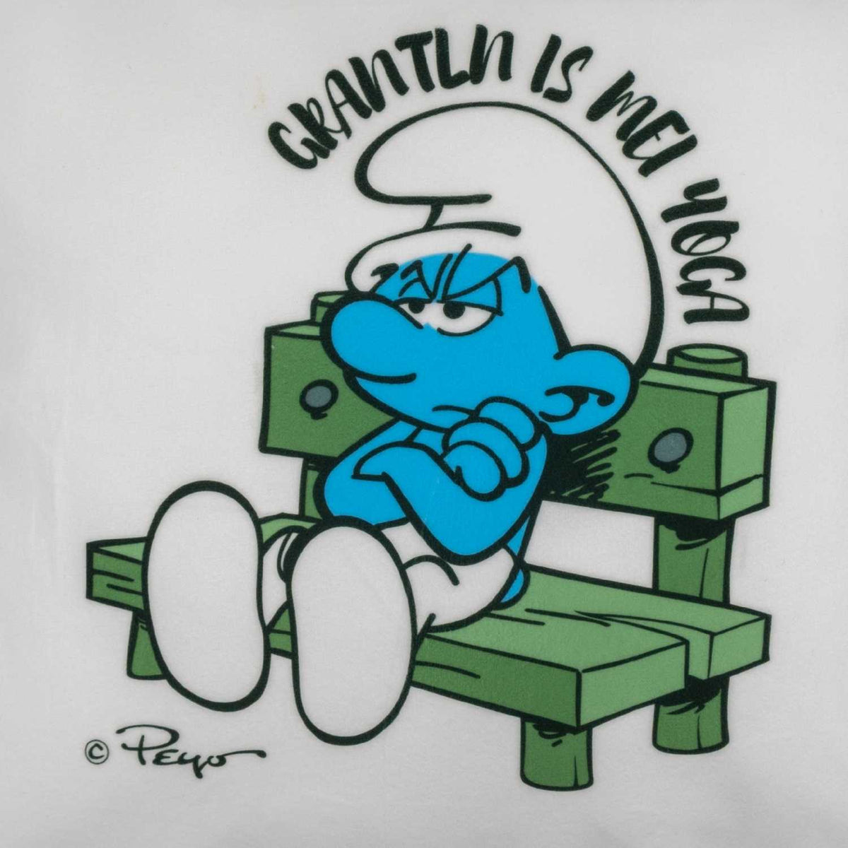 ®Die Schlümpfe "Grantln is mei Yoga" Kuschelkissen Motiv: Grantelbart Schlumpf sitzt grantig auf Bank.