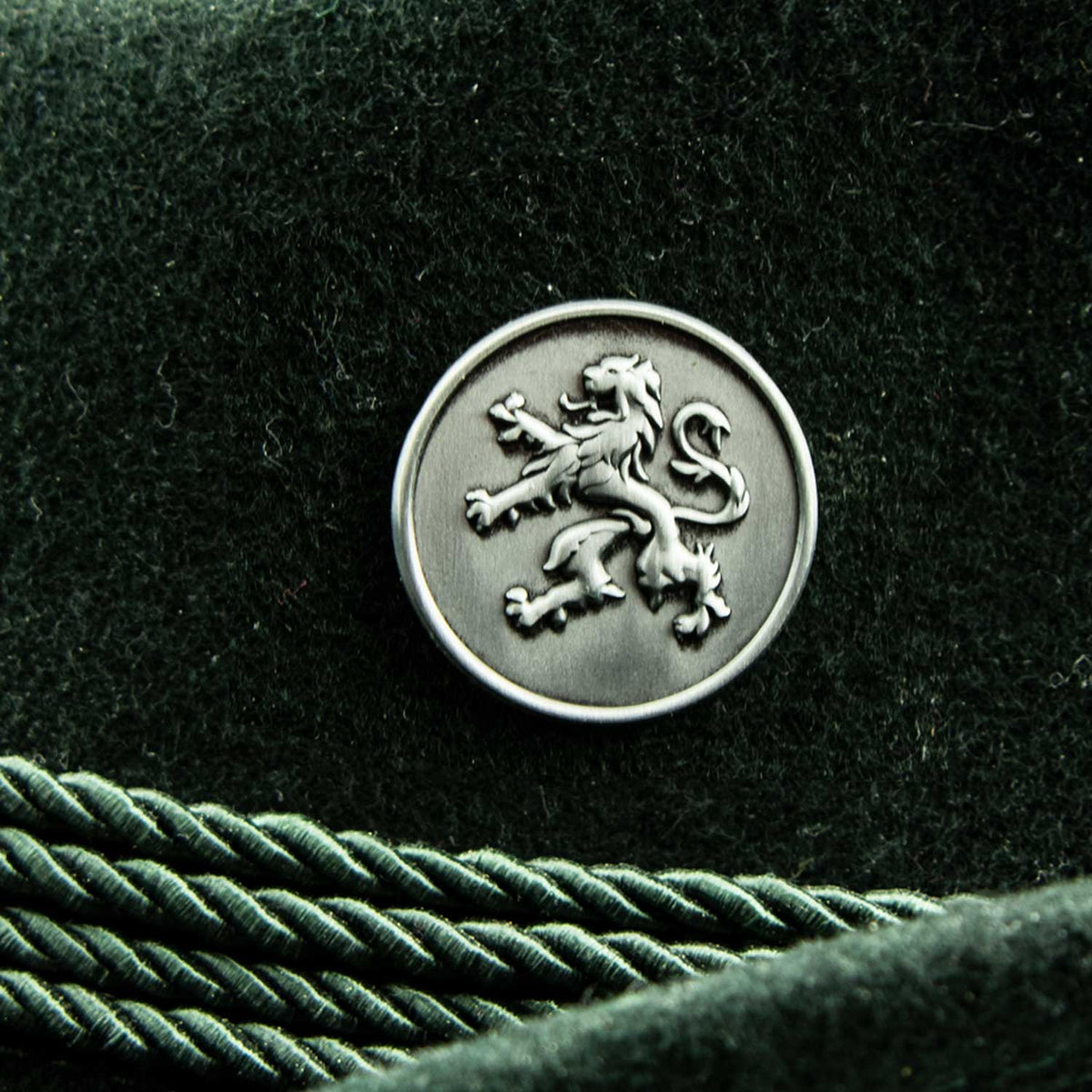 Silberner Metall Pin Löwe mit detaillierter Prägung auf dunklem grünem Filzstoff und Kordel.