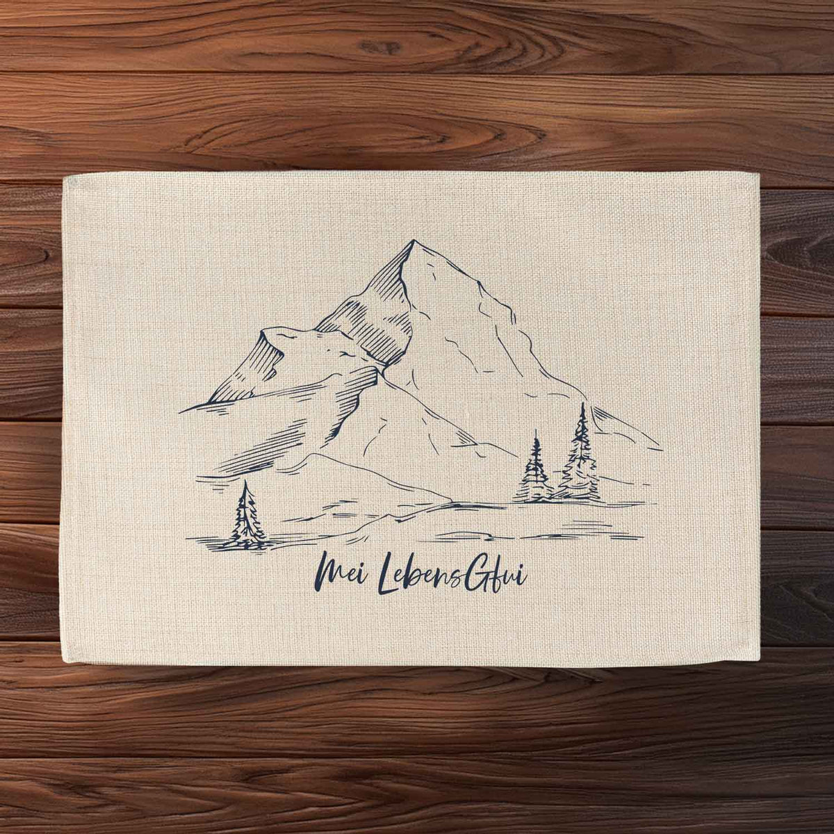 Tischset Landschaft mit detaillierter Bergkulisse und Tannenbäumen, dazu Mei LebensGfui Schriftzug auf Stoff.