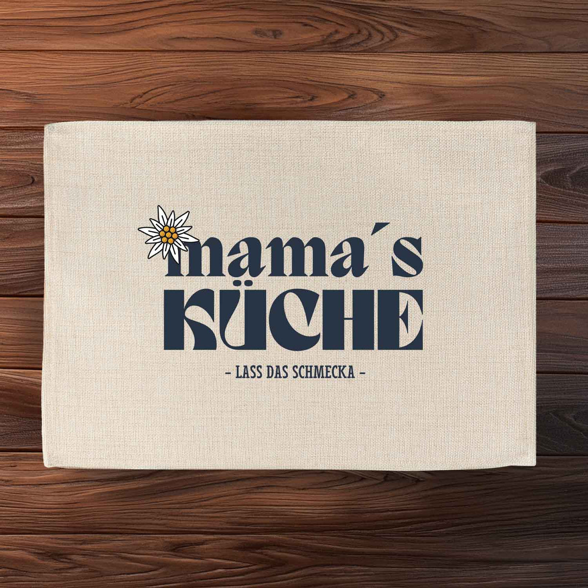 Beigefarbenes Tischset Mama's Küche auf Holztisch mit Edelweiß-Dekor und Spruch Lass das Schmecka