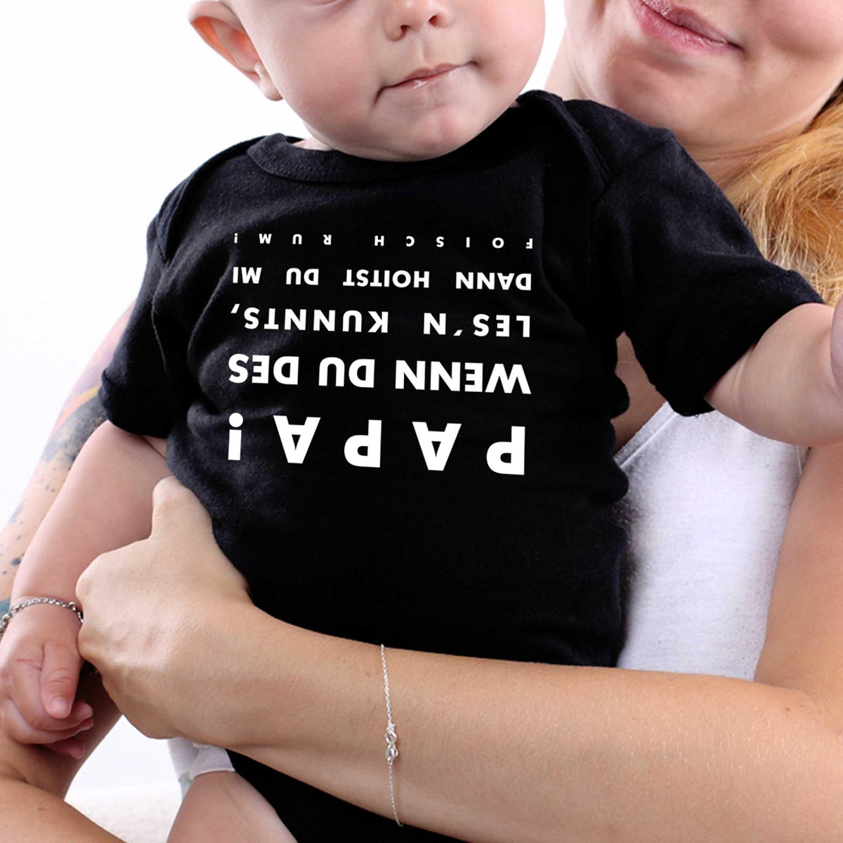 Baby Body falsch rum in Schwarz mit witzigem, umgedrehtem Spruch Papa! getragen von einem Baby im Arm.