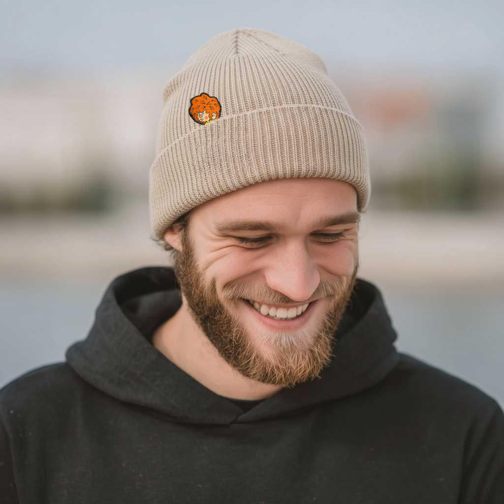 Lachender Mann trägt beigefarbene Pumuckl Beanie aus Baumwolle mit Stickmotiv am Strand.