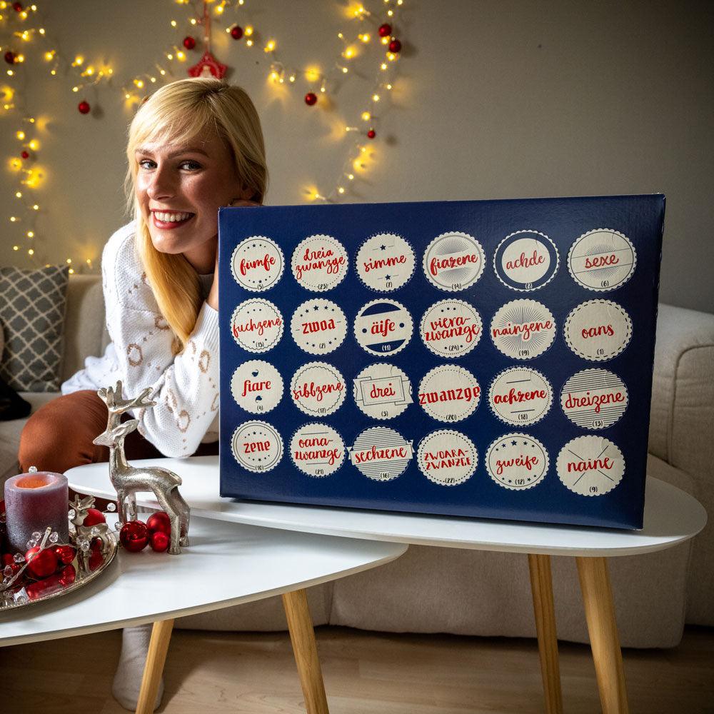 Lachende junge Frau hält ein blaues Adventskalender-Box mit runden Fächern und deutschen Mundart-Zahlen.