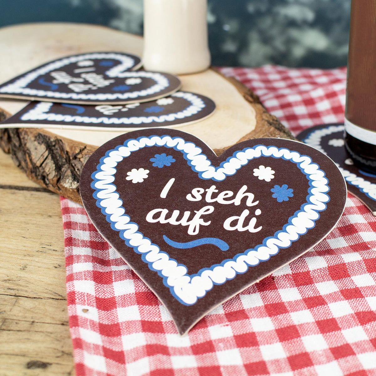 Bierfuizl-Lebkuchen-Herz mit Aufschrift "I steh auf di" auf rot-weiß karierter Serviette und Holzunterlage.