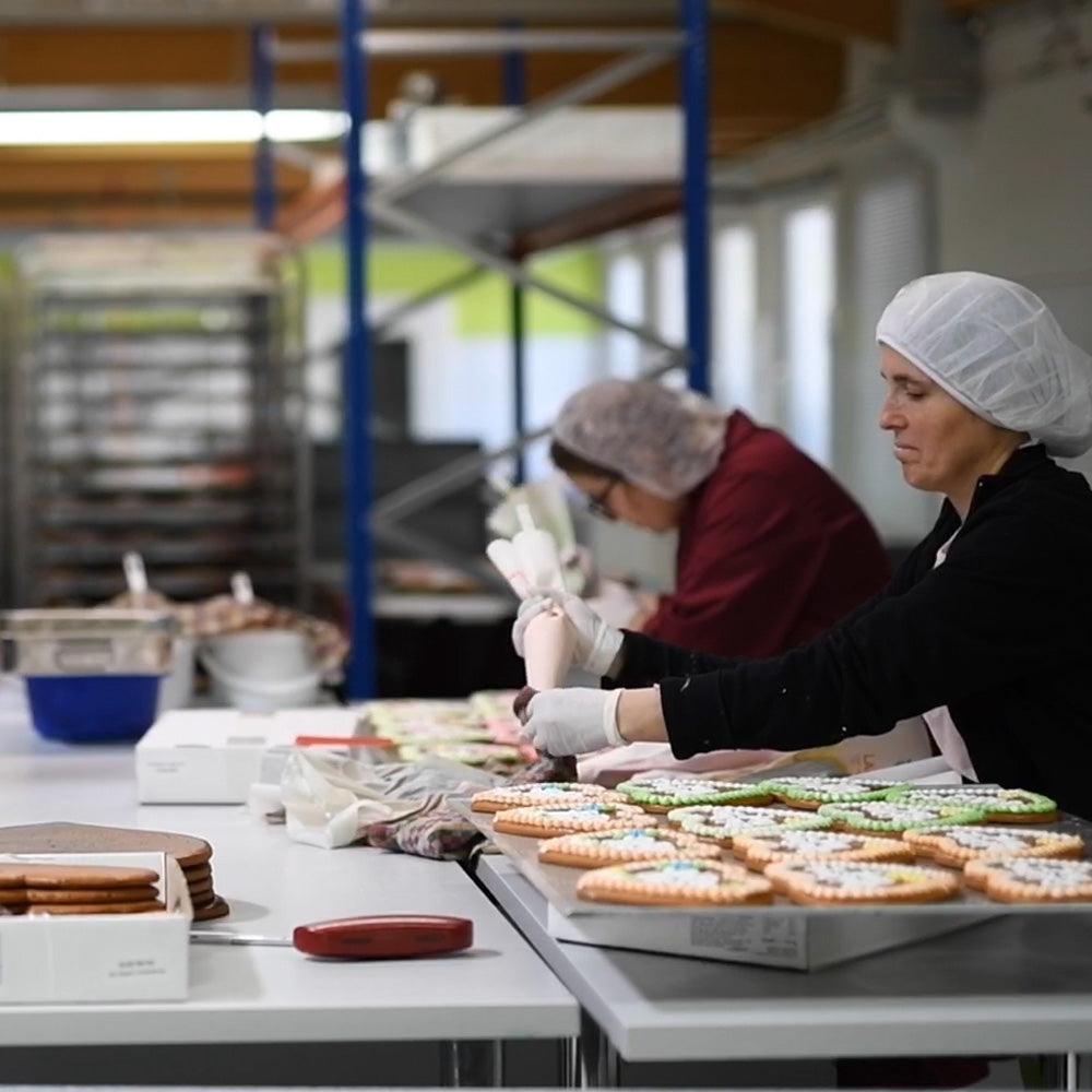 Bäckerinnen dekorieren handgefertigte Lebkuchen mit Zuckerguss in einer Backstube in Manufaktur-Qualität.