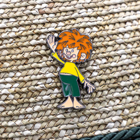 Pumuckl Servus Pin mit winkender Hand, auf hellem Korbgeflecht.