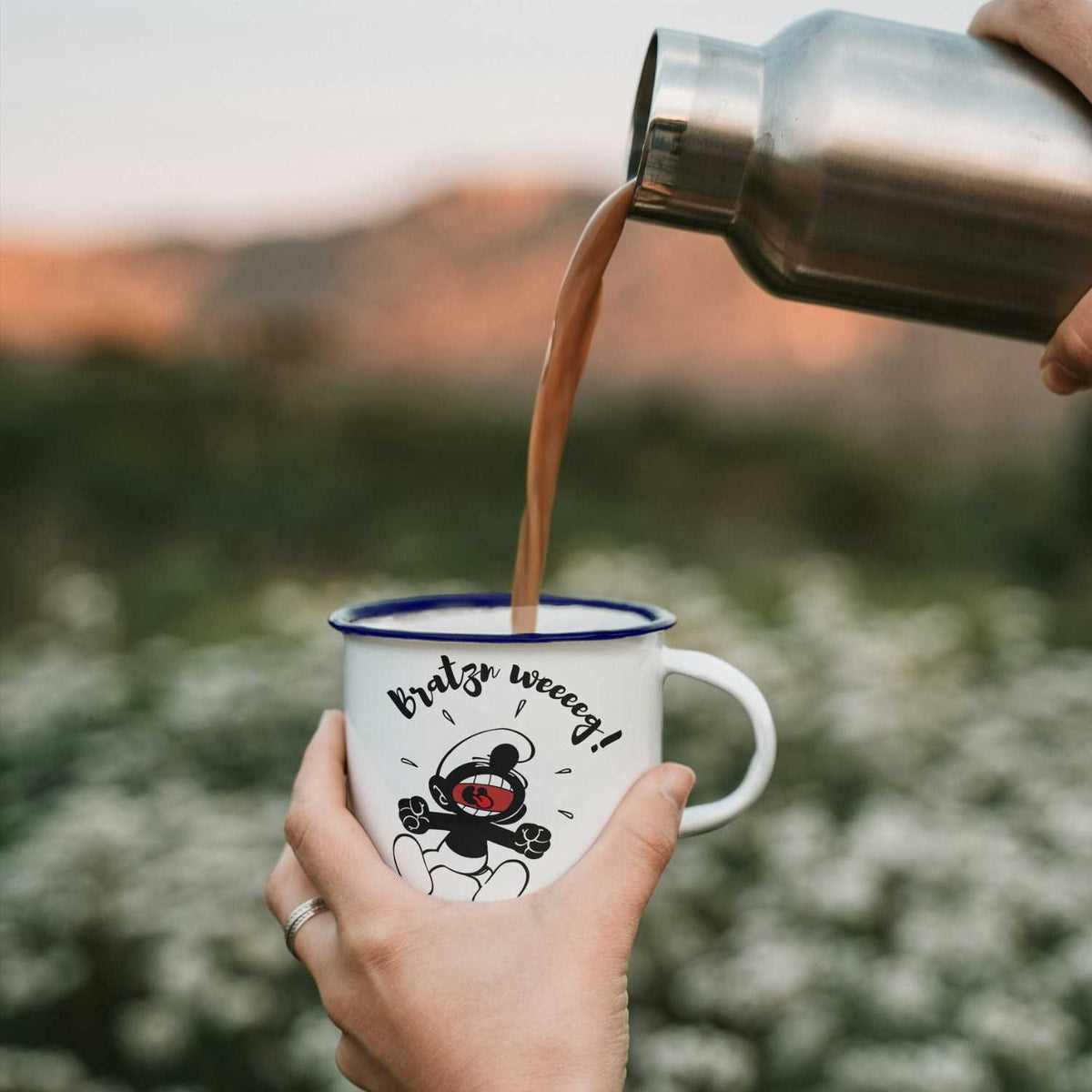 Emailletasse Die Schlümpfe Bratzn weg! wird von Thermoskanne mit heißem Getränk befüllt, Campingtasse.