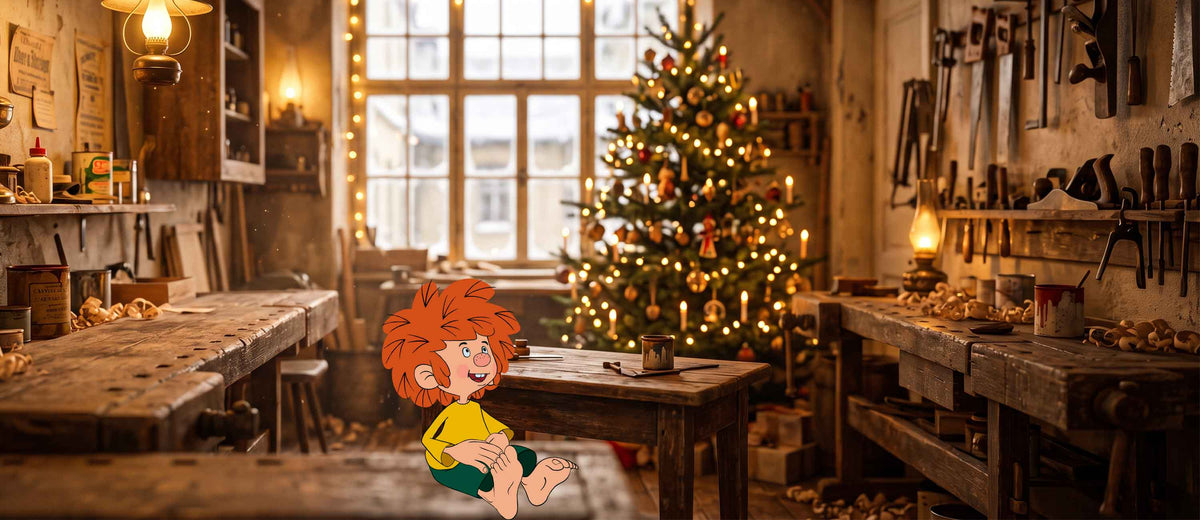 Pumuckl sitzt lachend in gemütlicher Weihnachts-Werkstatt mit leuchtendem Christbaum als Deko und Geschenkidee.