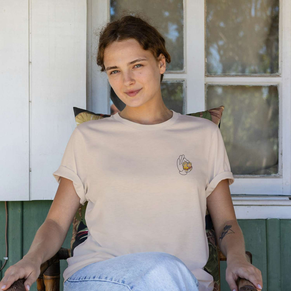 Junge Frau trägt hellbeiges Damen Rezept T-Shirt Lewakaas mit Leberkas-Motiv, auf Stuhl sitzend.