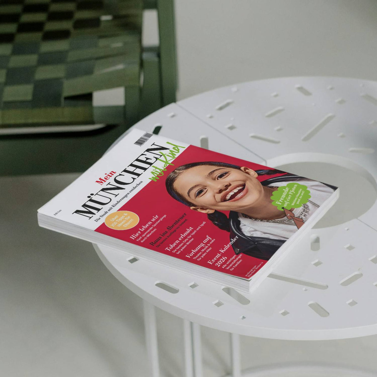 Magazin Mein München mit Kind auf weißem runden Tisch, Titelbild lächelndes Mädchen. Familienführer 2026.