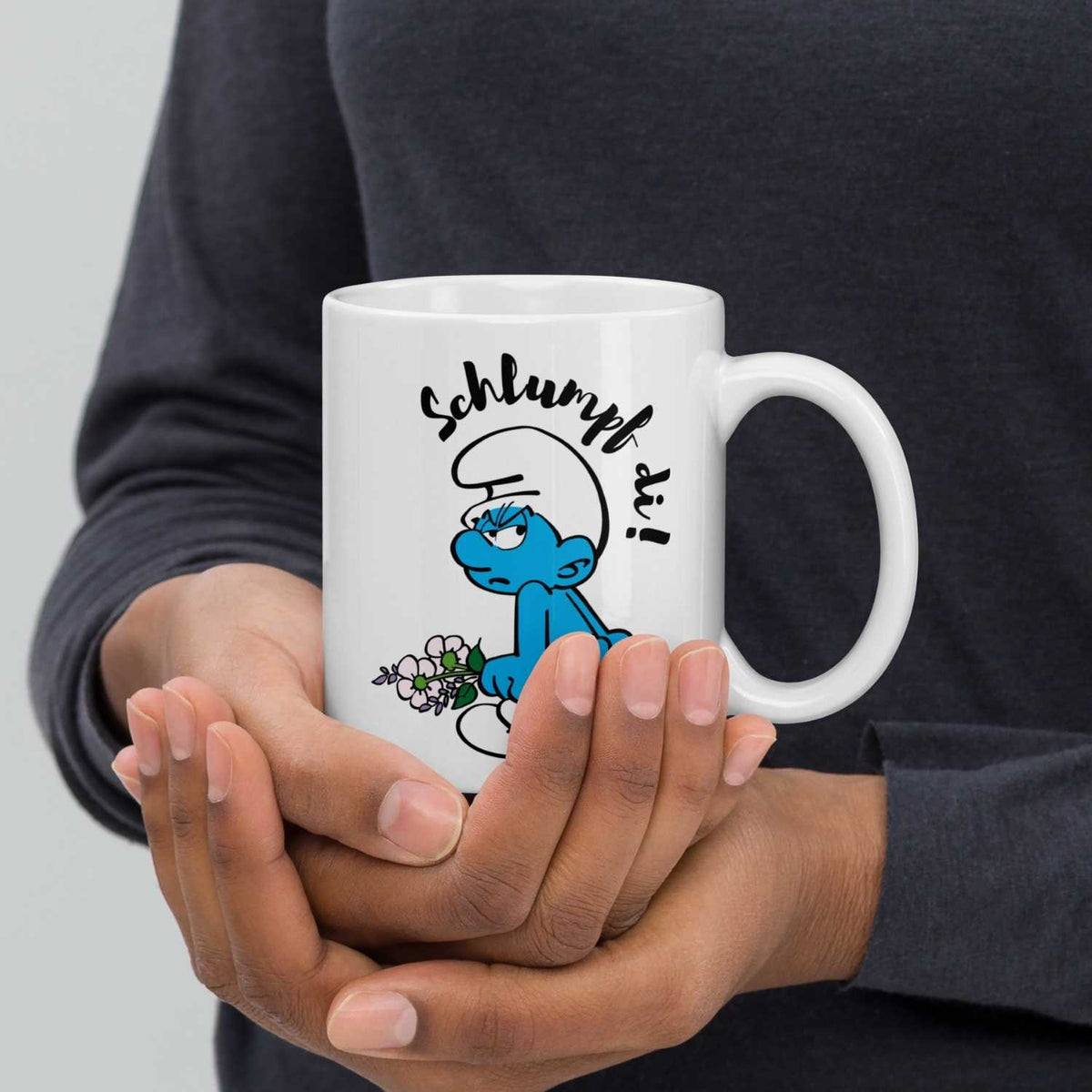 Person hält Schlumpf di! Tasse mit grummeligem Schlumpf und Blumen, weißer Keramikbecher, Markenware.
