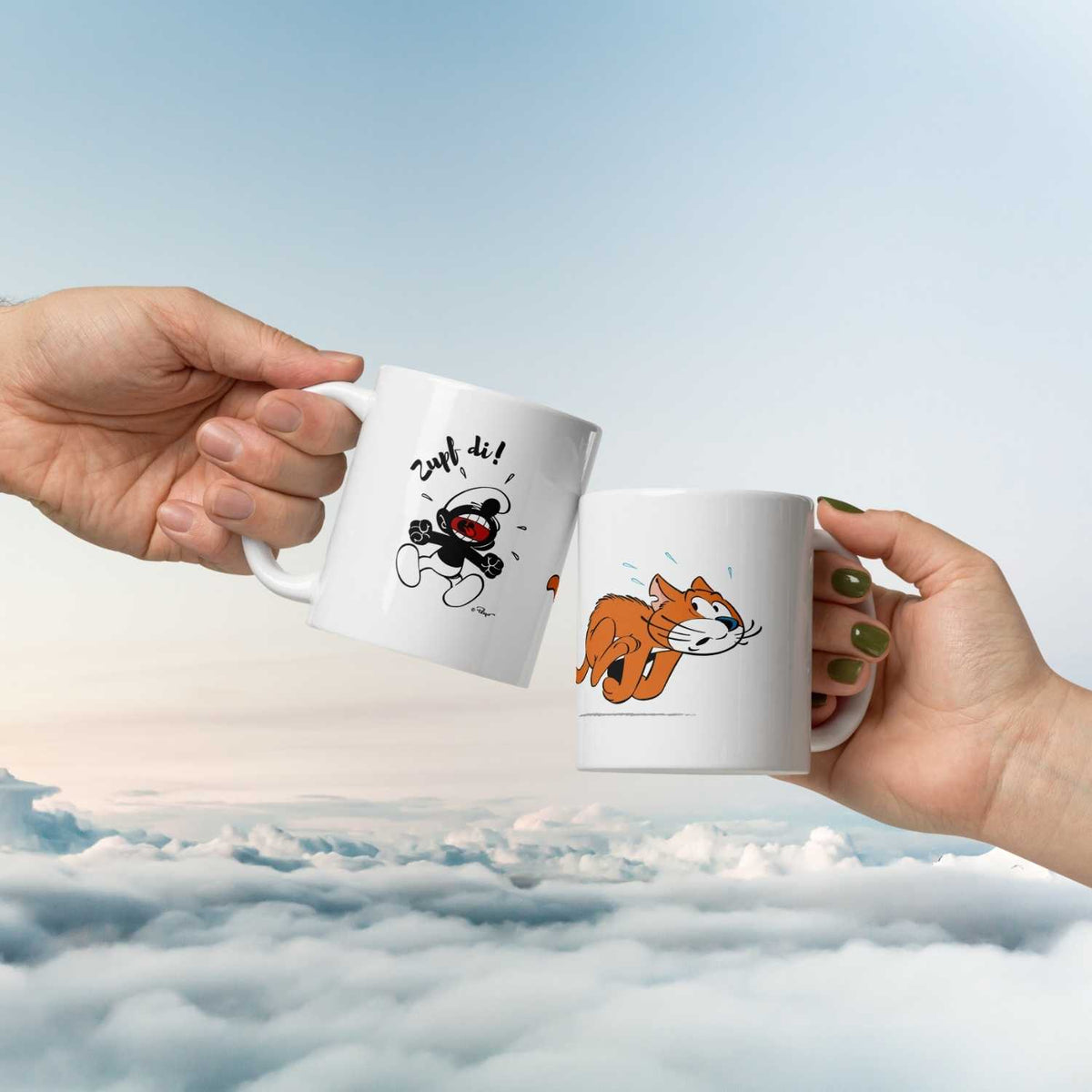 Hände stoßen mit ®Die Schlümpfe Tasse Zupf di! und Katze-Tasse vor blauem Himmel über Wolken an.