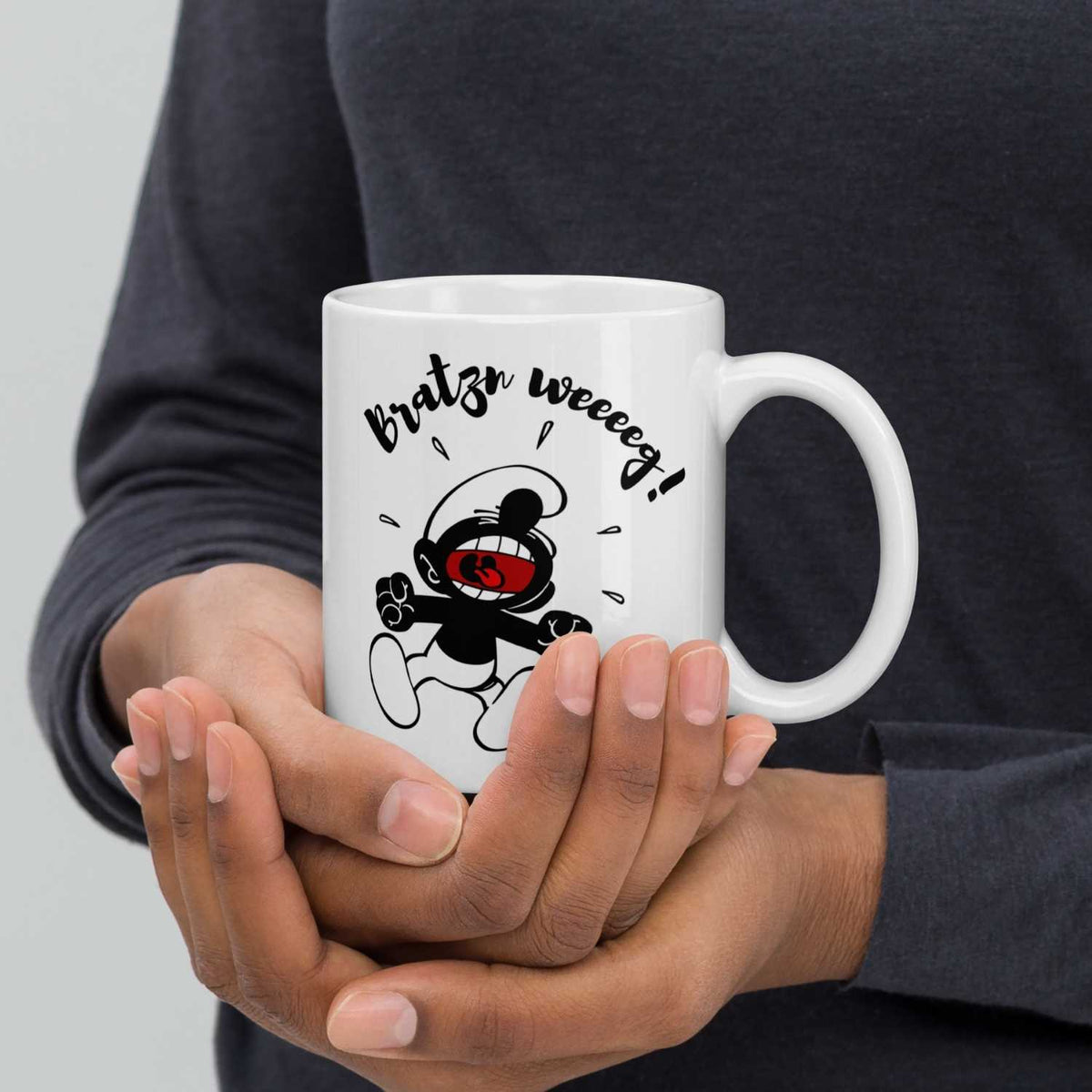 Hände halten eine weiße ©Die Schlümpfe Tasse "Bratzn weg!" mit lachendem Schlumpf-Motiv in Schwarz-Weiß.