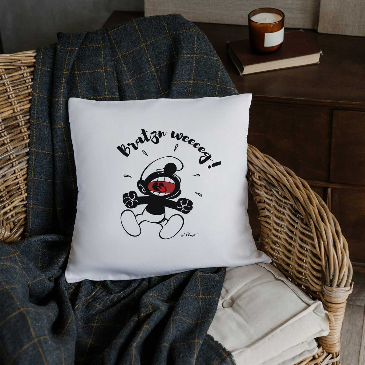 Weißes ®Die Schlümpfe "Bratzn weeeeg!" Kuschelkissen mit lustigem Schlumpf-Motiv auf gemütlichem Rattanstuhl.