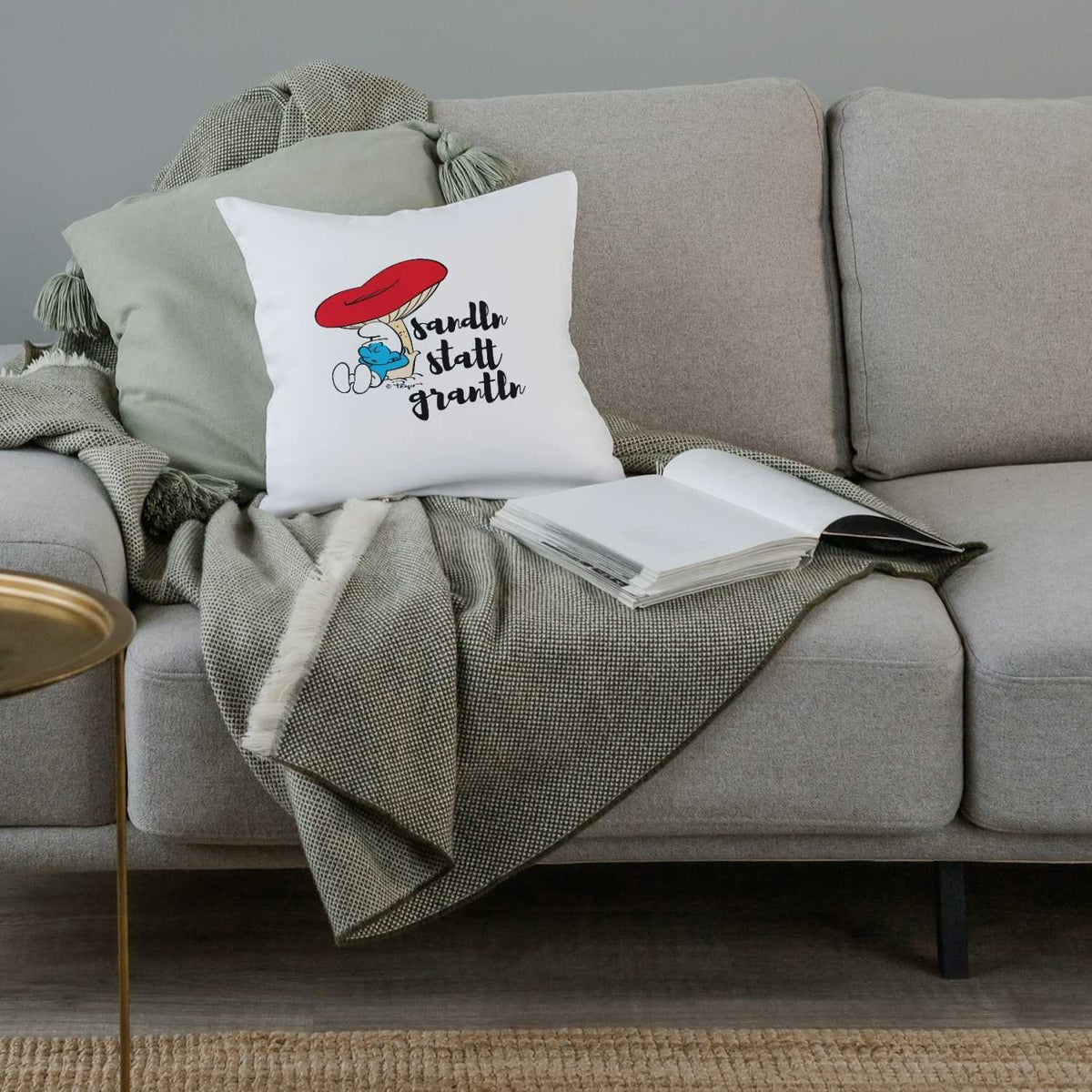 ®Die Schlümpfe Sandln statt grantln Kuschelkissen auf modernem grauen Sofa mit Decke und Buch.