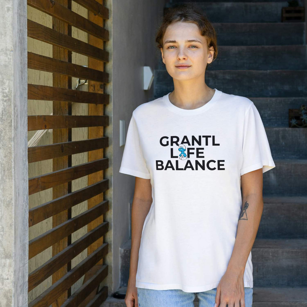 Frau trägt weißes Schlümpfe Damen T-Shirt Grantl Life Balance, bedruckt mit blauem, grantelndem Schlumpf.