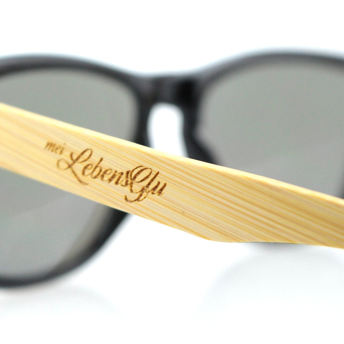 Detailansicht einer Sonnenbrille mit braunem Holzbügel und dem Schriftzug "mei LebensGfu" in eleganter Schrift