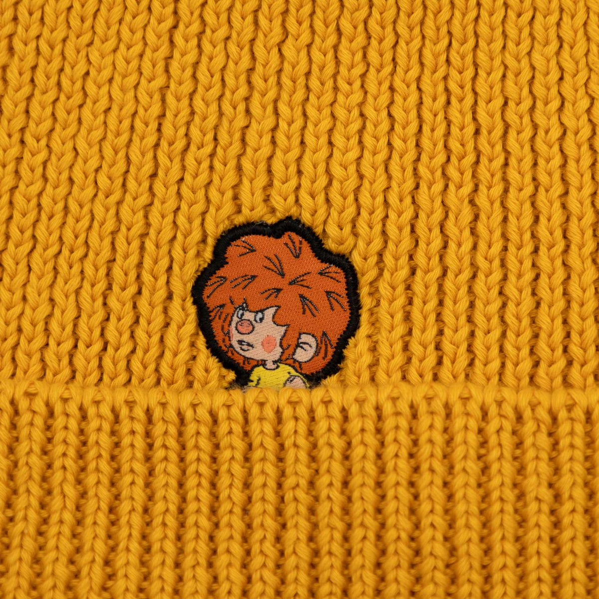 Nahaufnahme der gelben Pumuckl Beanie aus Baumwolle mit einem gestickten Pumuckl-Motiv.
