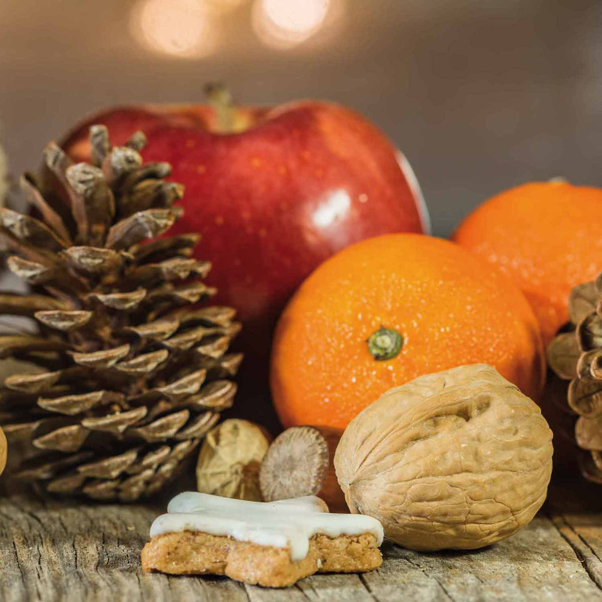 Weihnachtliche Stillleben-Arrangement mit Zimtstern, Apfel, Mandarinen und Walnüssen auf rustikalem Holz.