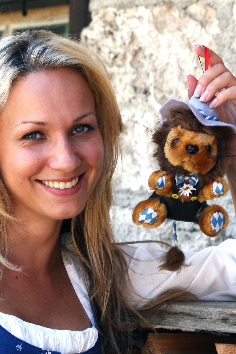 Lächelnde Frau im Dirndl hält einen plüschigen bayerischen Löwen mit weiß-blau karierter Hose.
