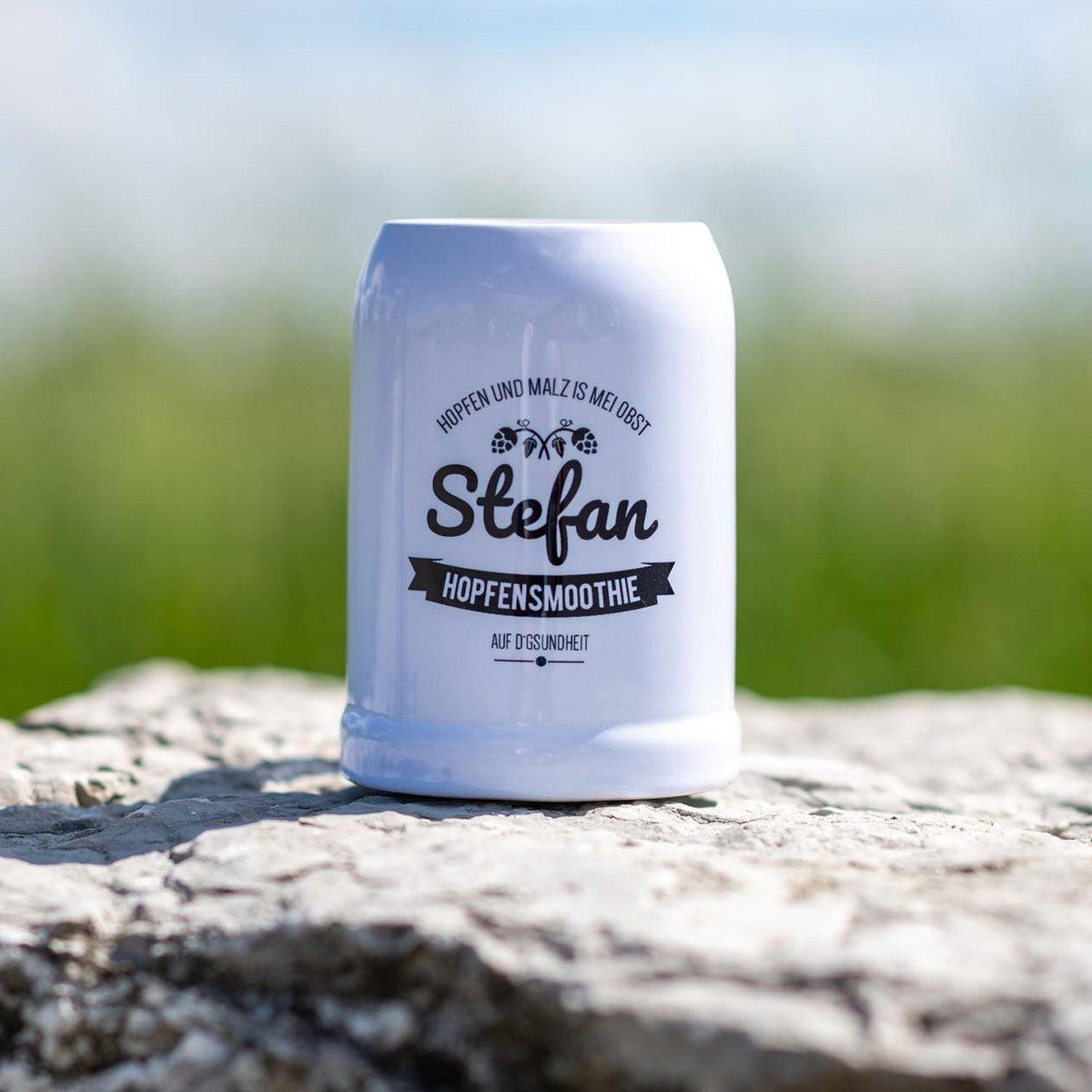 Weißer Keramik-Bierkrug mit schwarzem "Hopfensmoothie Stefan" Aufdruck auf steinernem Untergrund.