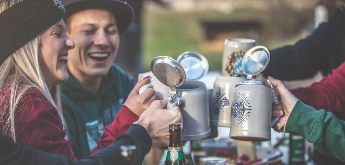 Freunde stoßen fröhlich mit traditionellen Bierkrügen aus Keramik und Zinndeckel an.