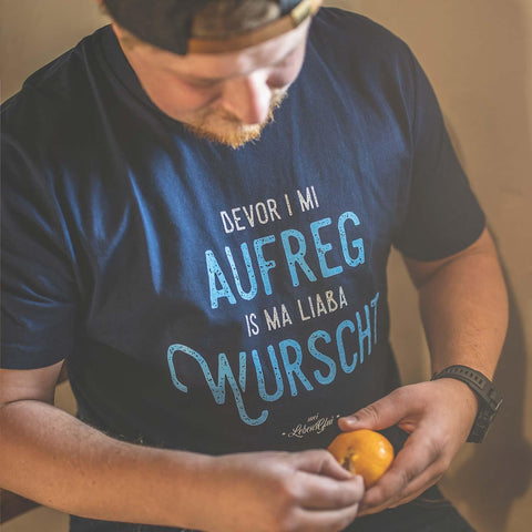 Herren T-Shirt „Bevor i mi aufreg, is ma liaba wurscht“ in Dunkelblau, getragen von einem Mann mit Bart