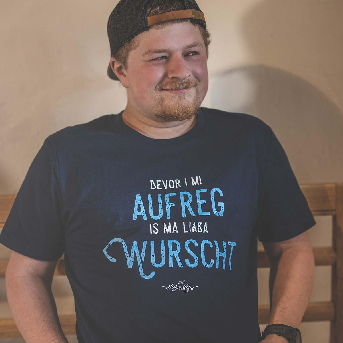 Lachender Mann mit Baseballcap im bayerischen T-Shirt „Bevor i mi aufreg, is ma liaba wurscht“