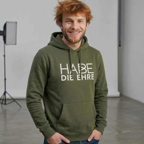 Lächelnder Mann mit rotem Haar trägt olivgrünen Hoodie Habe die Ehre Aufdruck und Kapuze.