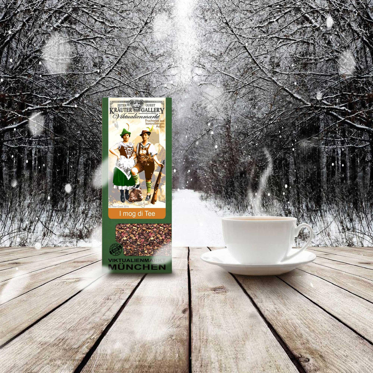 Grüne Teepackung mit bayerischem Motiv, daneben dampfende Teetasse auf Holztisch vor verschneitem Winterwald.
