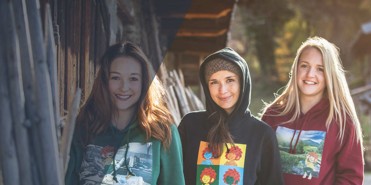 Drei lächelnde Frauen in Hoodies mit lustigen Cartoon-Prints und Bergmotiven, im Freien.