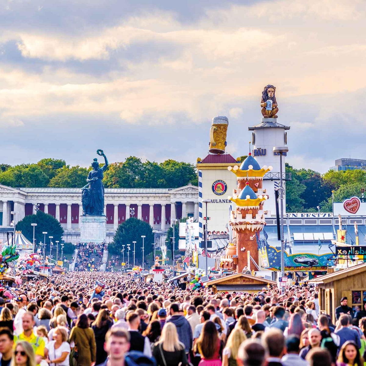Vielbesuchtes Münchener Oktoberfest Gelände mit Bavaria-Statue, Theresienwiese und Festzelten bei Tageslicht.
