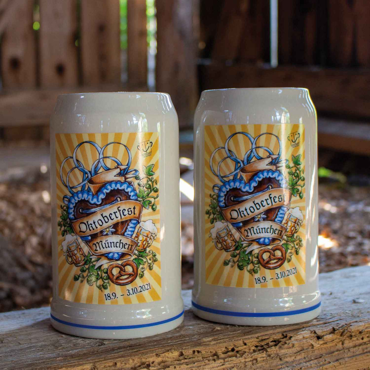 Zwei Oktoberfest München Bierkrüge aus Keramik mit traditionellem Herzmotiv, Brezel und Hopfen-Dekor.