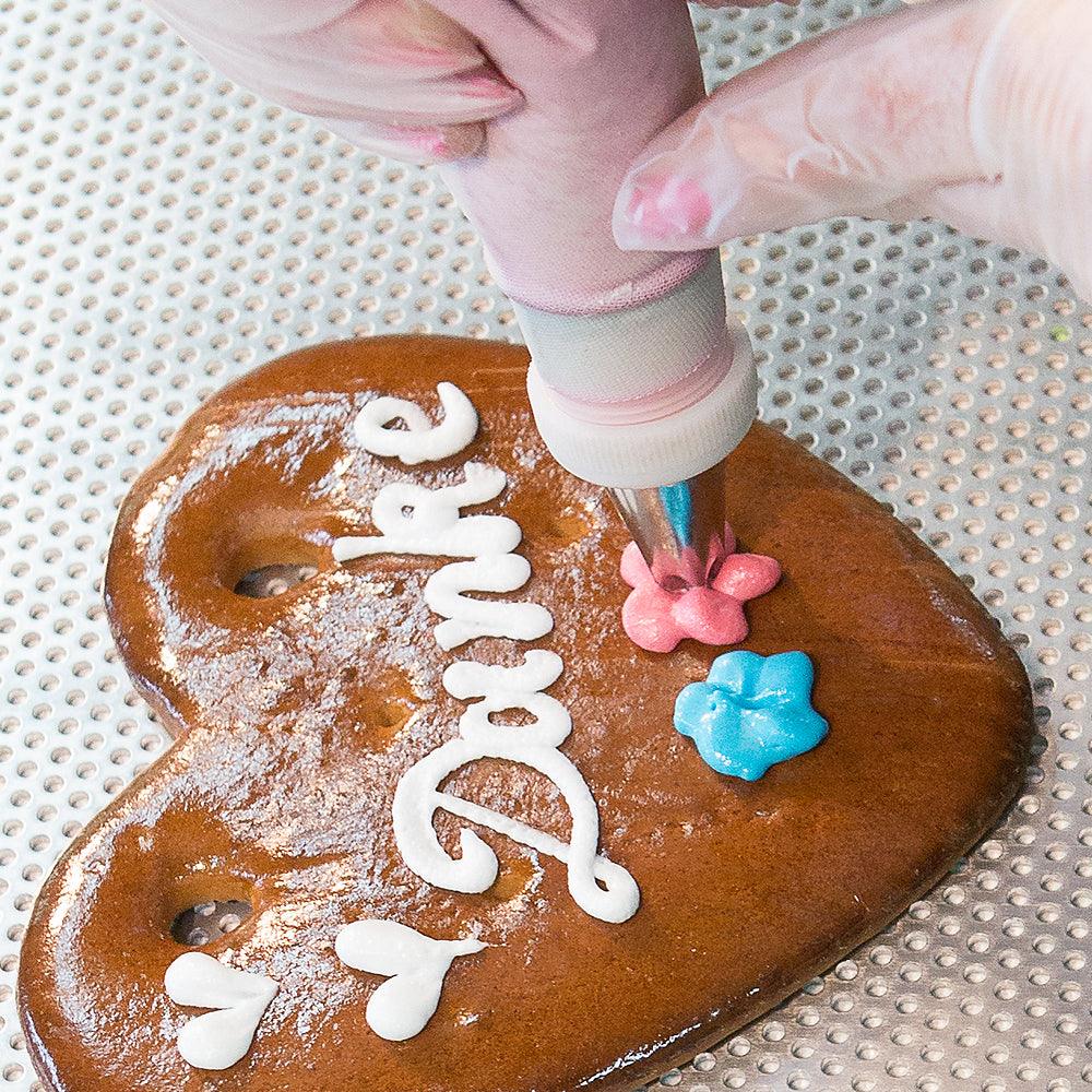 Lebkuchenherz mit Schriftzug "Danke", verziert mit bunter Zuckerguss-Blumen von einer Spritztüte.