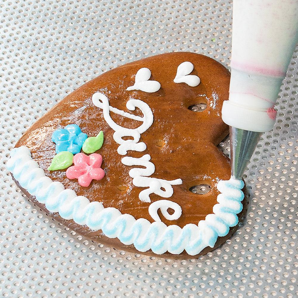 Braunes Lebkuchenherz mit weißer "Danke"-Aufschrift, bunten Zuckergussblumen und blau-weißem Rand.