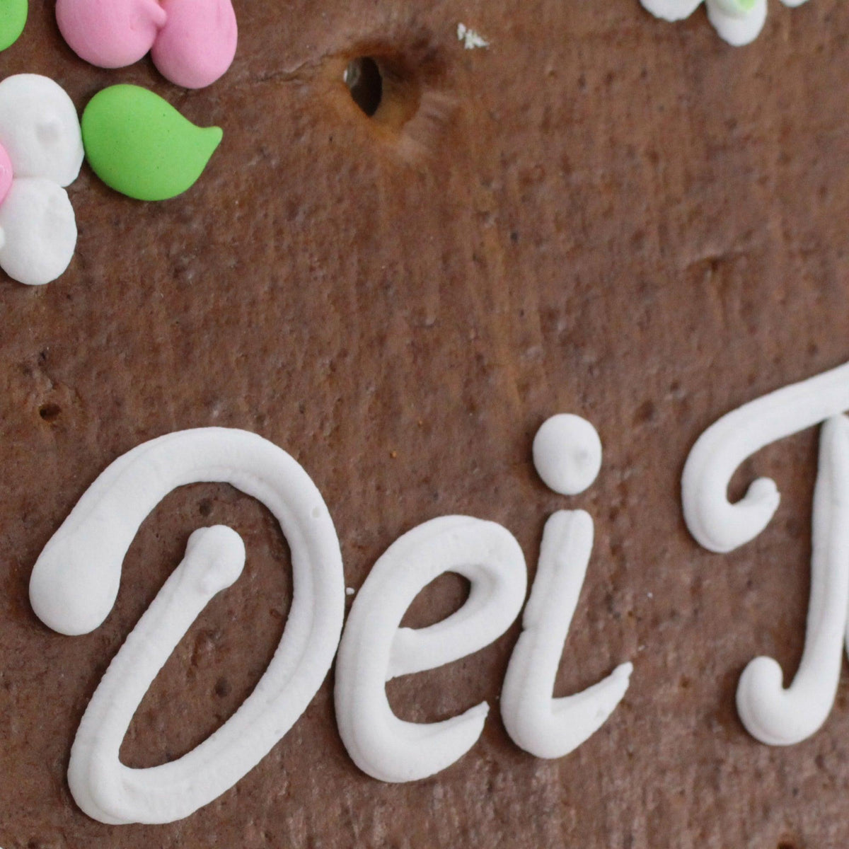 Detailansicht eines Lebkuchenherzens mit weißer Zuckerglasurschrift Dei und bunten Zuckerblumen.