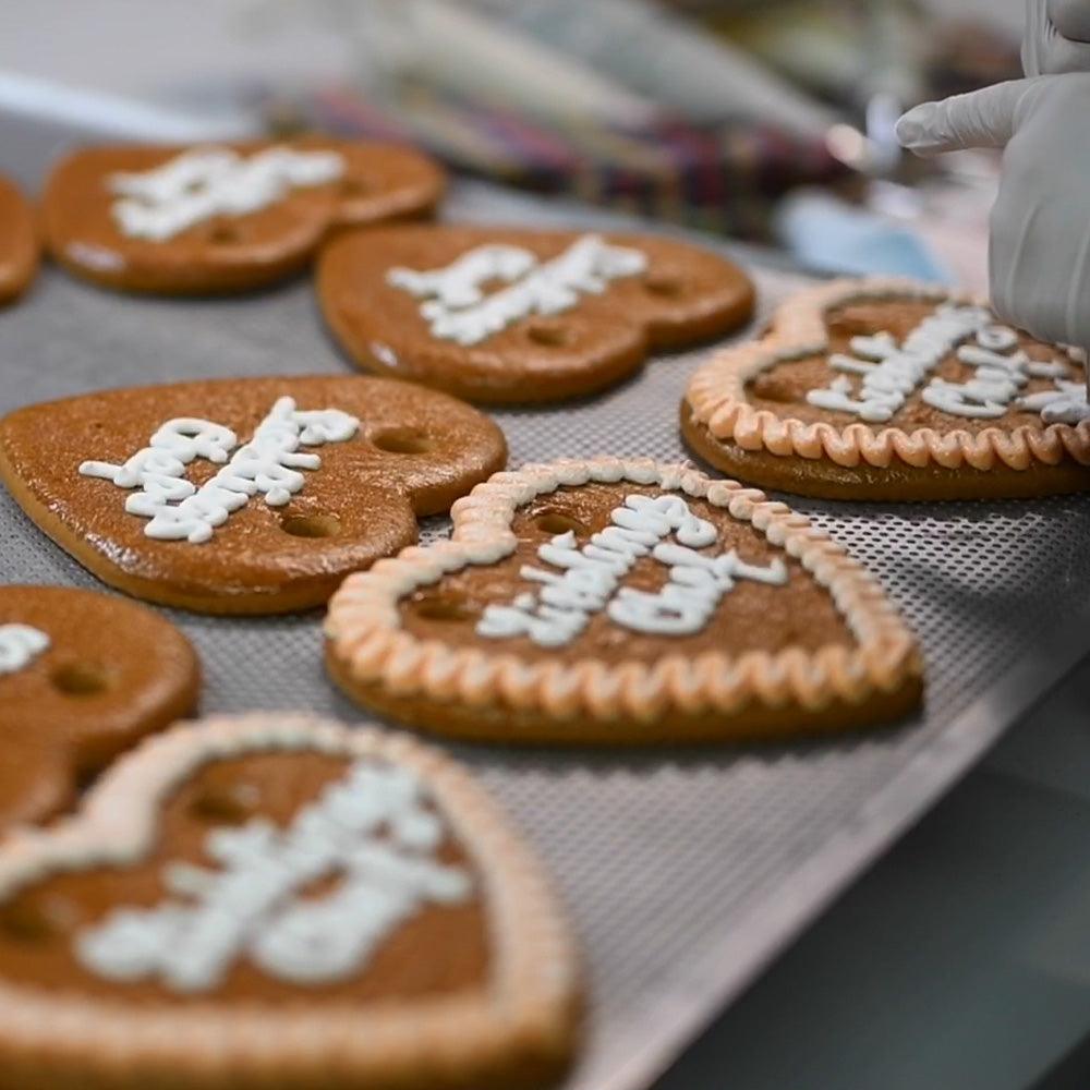 Bäckerei verziert handgemachte Lebkuchenherzen mit Zuckerguss auf einem Backblech, bereit zum Verkauf.