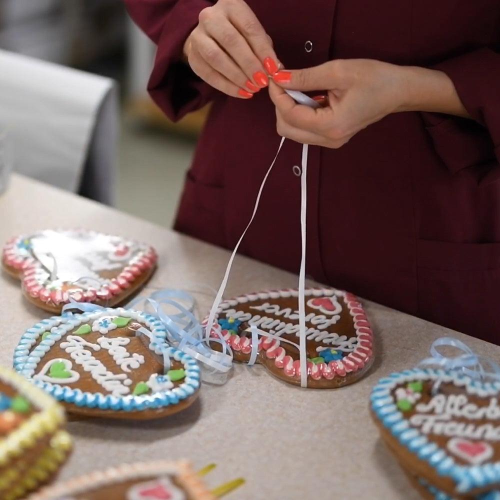 Hände binden blaues Band an Lebkuchenherzen mit individuellen Sprüchen und Zuckerguss-Verzierungen.