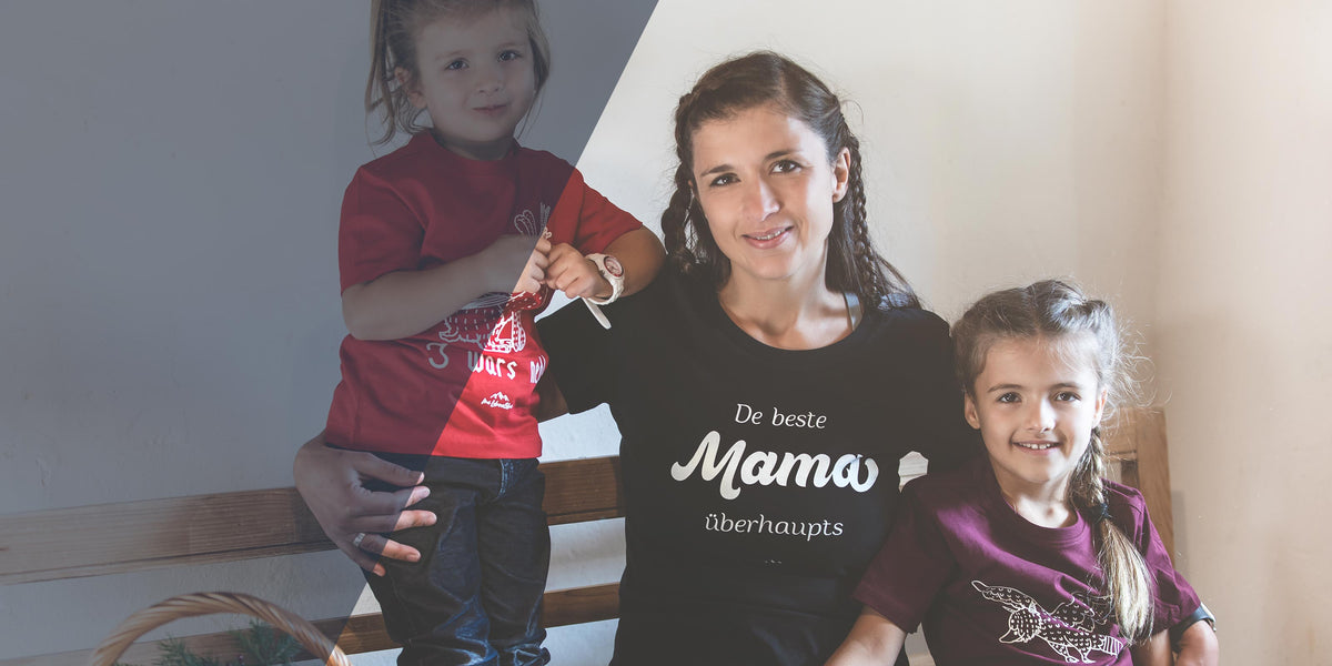 Glückliche Familie mit Mutter in schwarzem T-Shirt "De beste Mama überhaupt" und zwei lachenden Kindern.