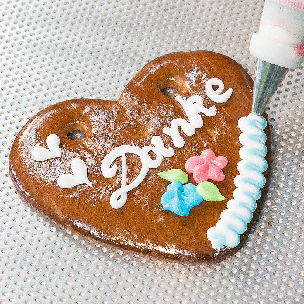 Nahaufnahme eines Lebkuchenherzens mit "Danke"-Aufschrift und bunter Zuckerglasur, dekoriert auf Lochblech.