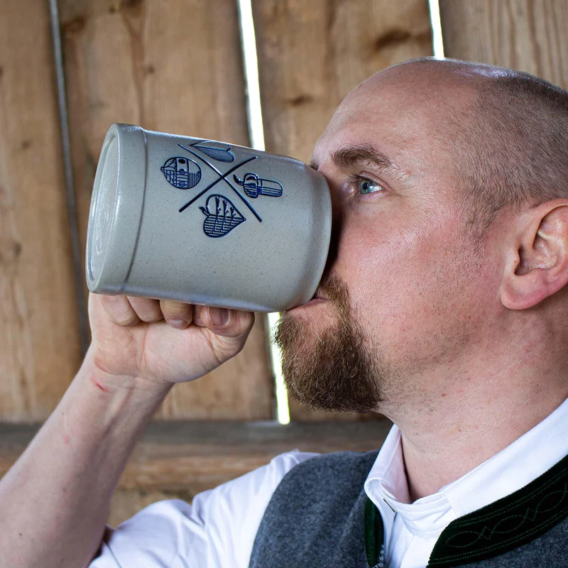 Mann in Tracht trinkt aus PREMIUM Bierkrug Schafkopfen aus Salzglasur mit bayerischem Kartenspiel-Motiv.