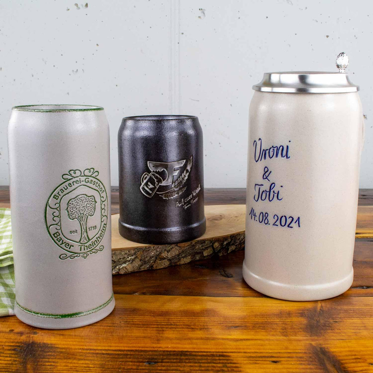 Diverse Bierkrüge: Sandfarbener Krug mit grünem Logo, schwarzer Krug mit Gravur und Keramikkrug mit Zinndeckel und personalisierter Aufschrift auf Holztisch.