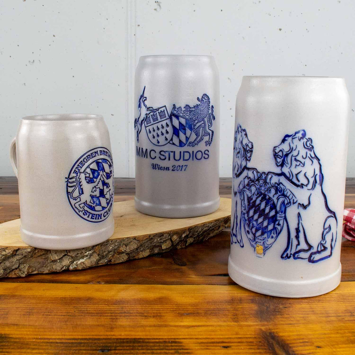 Verschiedene Steinbierkrüge aus Keramik mit blauen Wappen und Löwenmotiven auf rustikalem Holztisch.