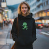 Junge Frau im schwarzen Hoodie mit grünem Pumuckl-Motiv, lässig auf einer belebten Straße posierend für E-Commerce.
