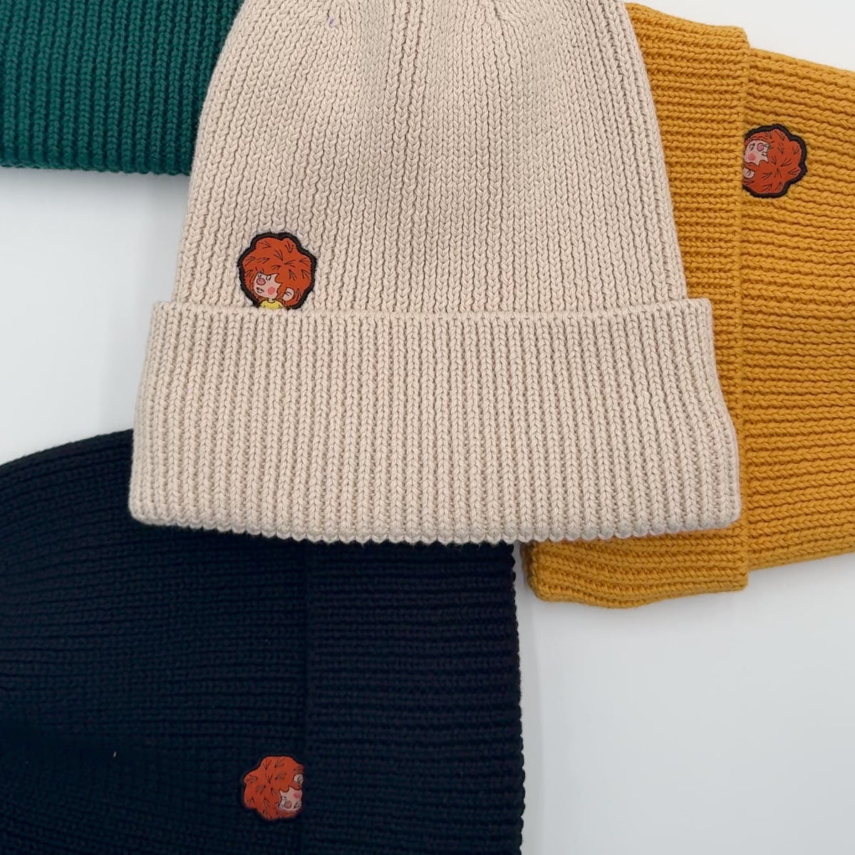Kollektion von Pumuckl Beanies in verschiedenen Farben: beige, senfgelb, dunkelblau und dunkelgrün aus Baumwolle.