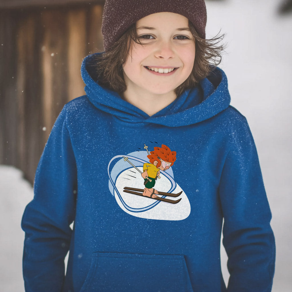 Fröhliches Kind in blauem Pumuckl Kinder Hoodie "Skifahren" mit rotem Kobold auf Skiern im Schnee.