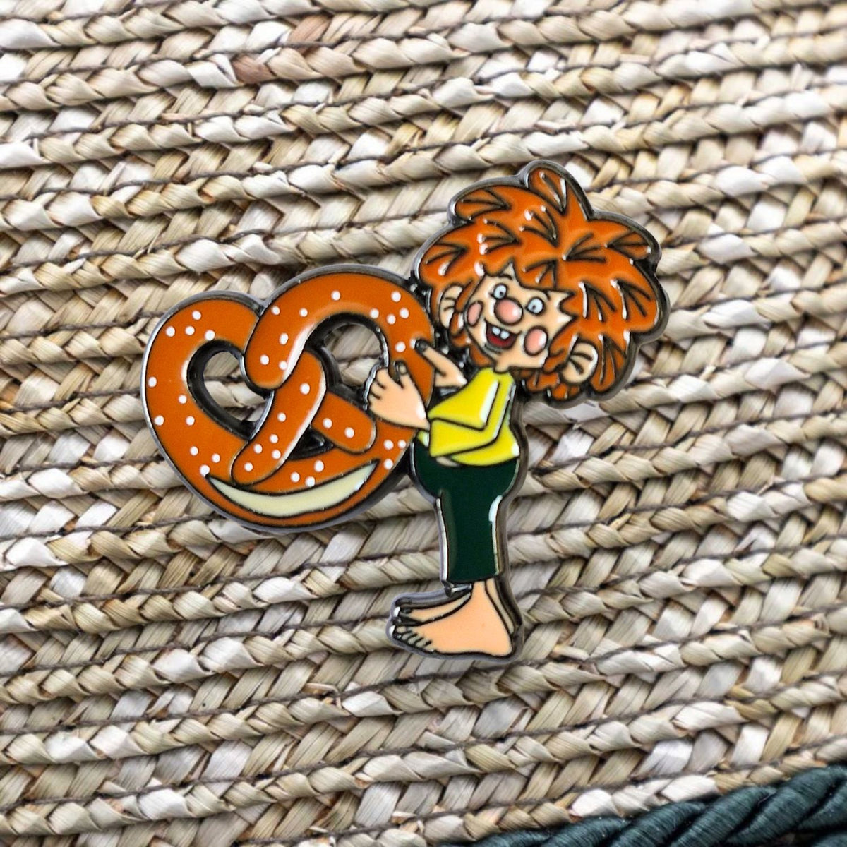 Pumuckl Pin Breze – Emaille Anstecker, Pumuckl umarmt eine gesalzene Brezel, auf geflochtenem Untergrund